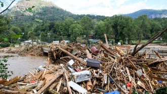 A pile of debris in water is pushed up against the side of a bridge.