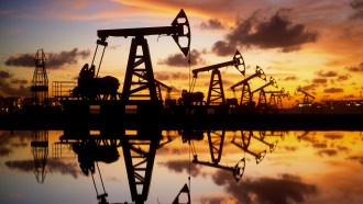 The silhouette of oil rigs among an orange and blue sky.